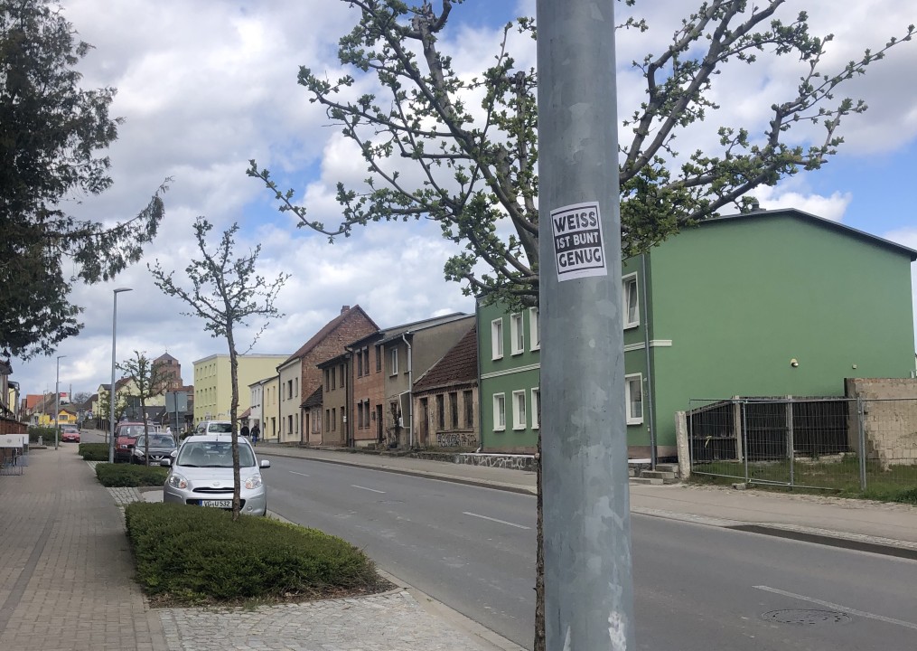 Straße im Wohngebiet, an einem Pfahl ein Aufkleber mit der Aufschrift: Weiss ist bunt genug.